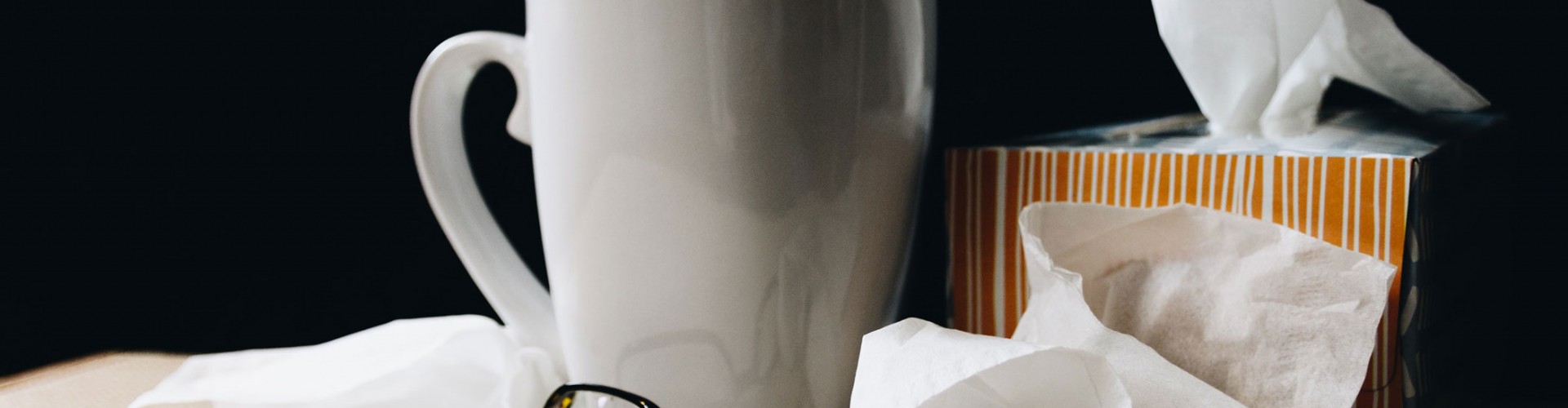 mug, spectacles and tissues at bedside, suggesting a cold or flu