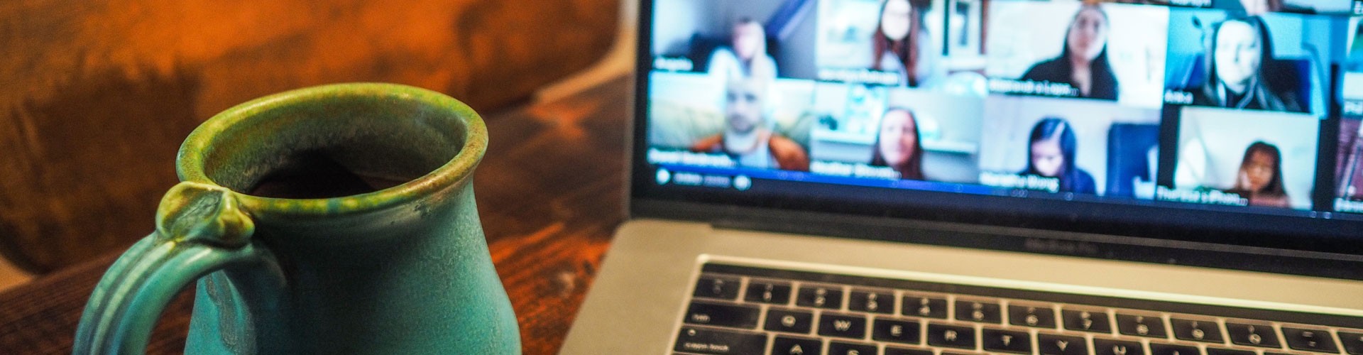 laptop with large online meeting and mug of coffee