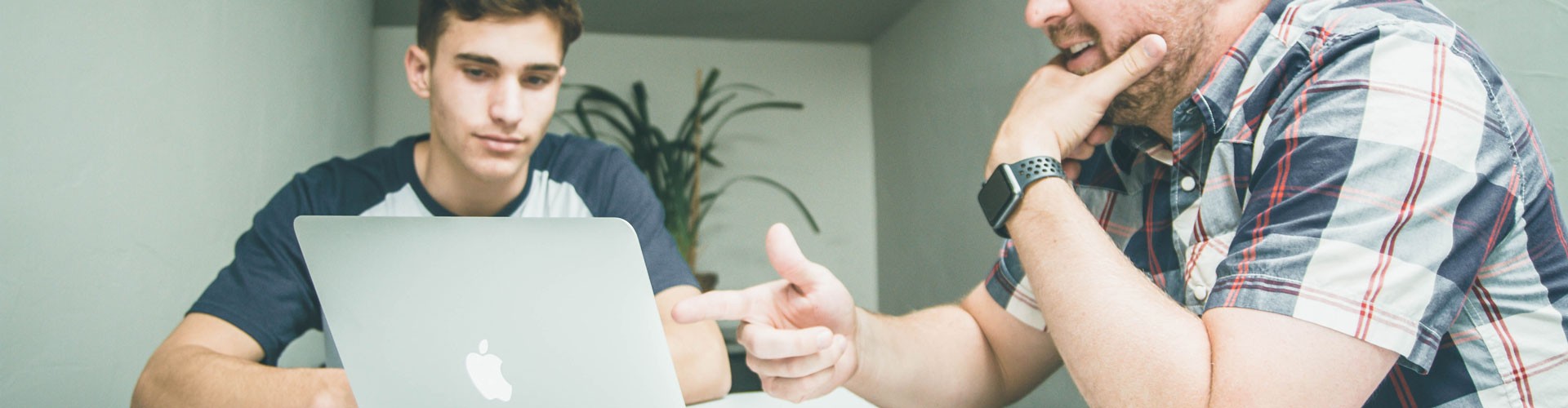 young man being shown something on a laptop by an older man