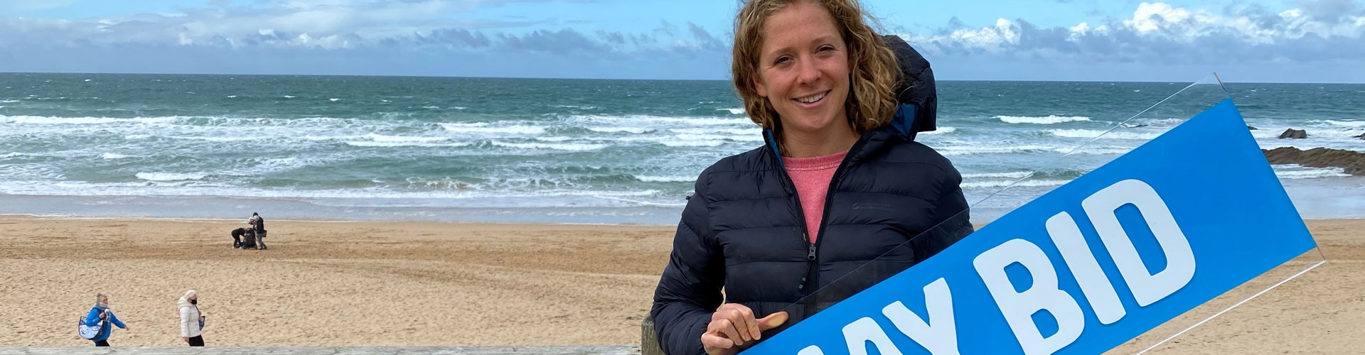 woman standing with seascape behind holding Newquay BID sign