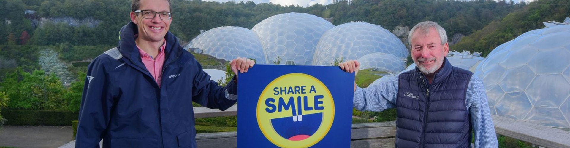 two men holding a sign in front of the biomes at the eden project