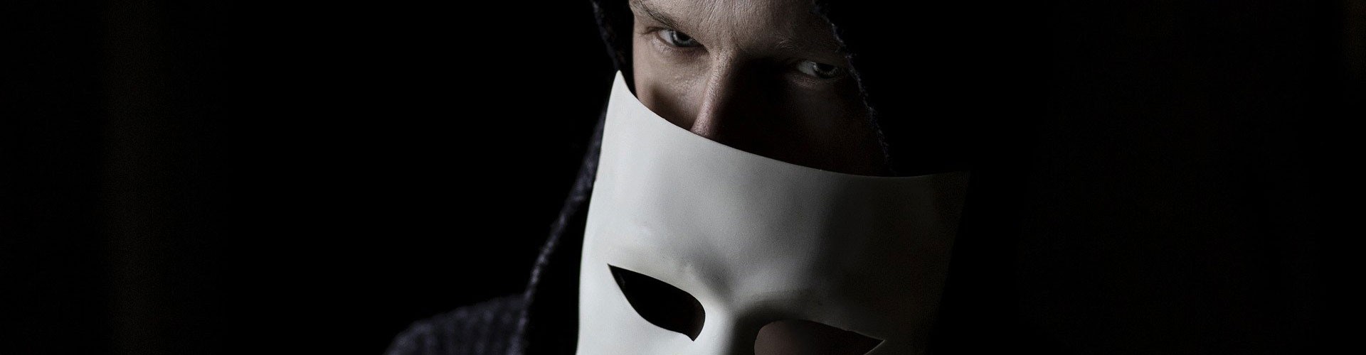 man in black hoodie holding white mask across face