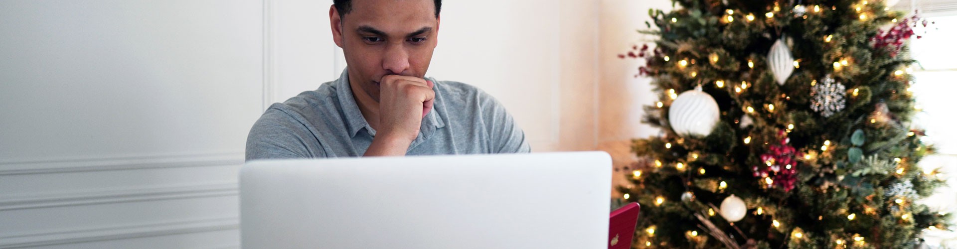 man looking at laptop with christmas tree in background