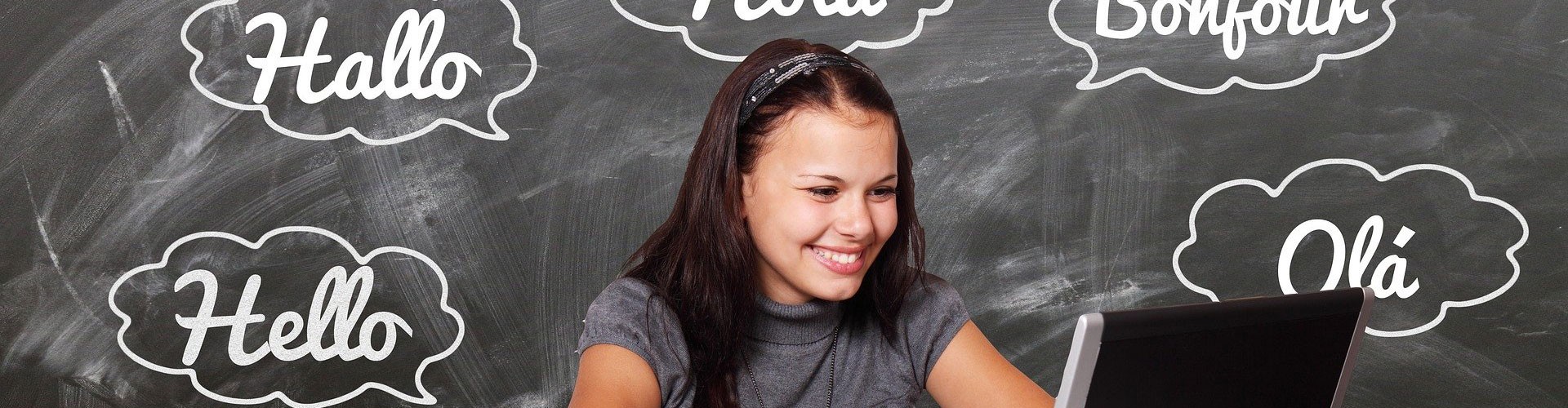 woman with laptop in front of a chalkboard with "hello" written in different languages