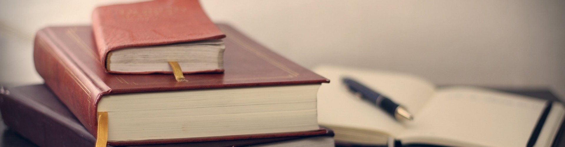 A pile of books with a pen resting on an open notebook in the background