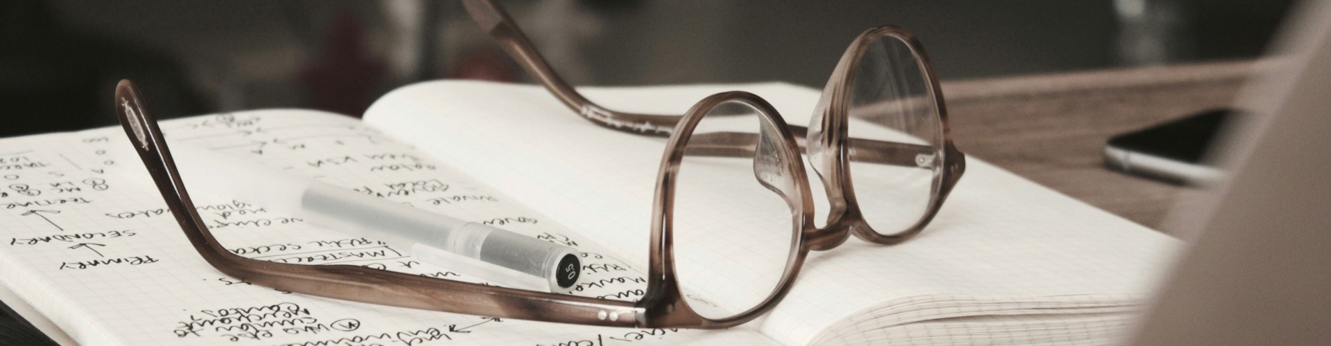 A pair of glasses and a white pen on a notebook