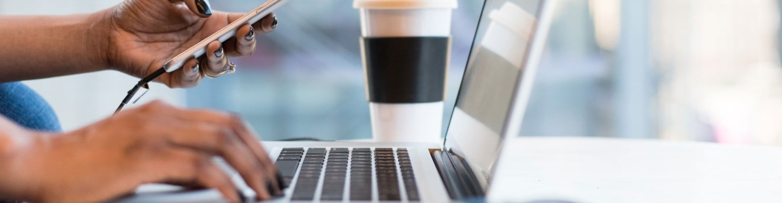 Hands using laptop and phone, coffee in the background