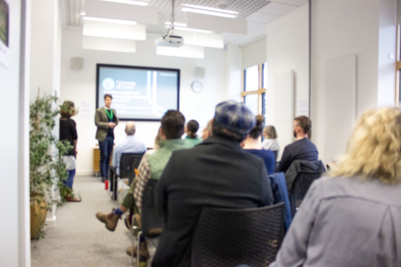 Out-of-focus-aesthetic image of a room of people listening to academic Philipp Thies who is presenting on the topic of Floating Offshore Wind and the skills gaps that will need to be covered in the upcoming years. Mary Hesling, project manager is to Philipp's left.