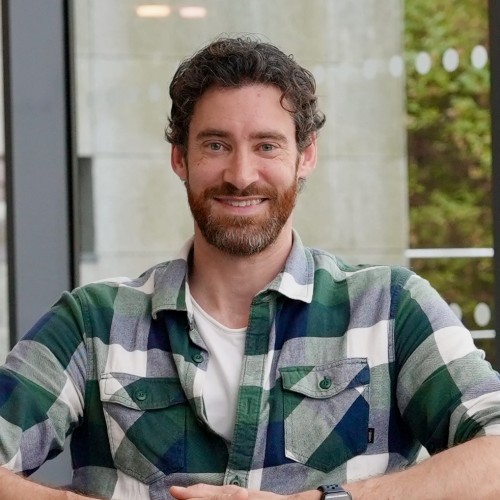 Image shows a man with a green plad shirt looking at the camera.