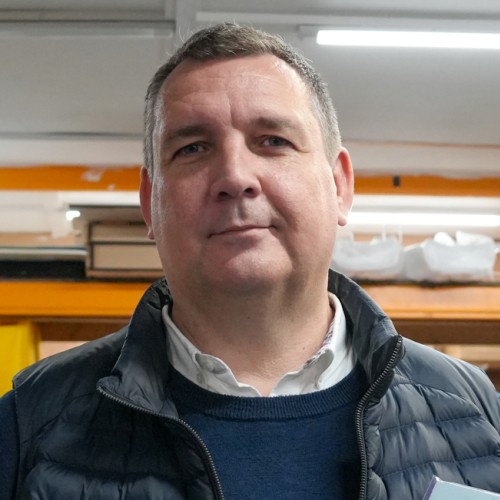 A person in a blue Gillet with orange shelves in the background